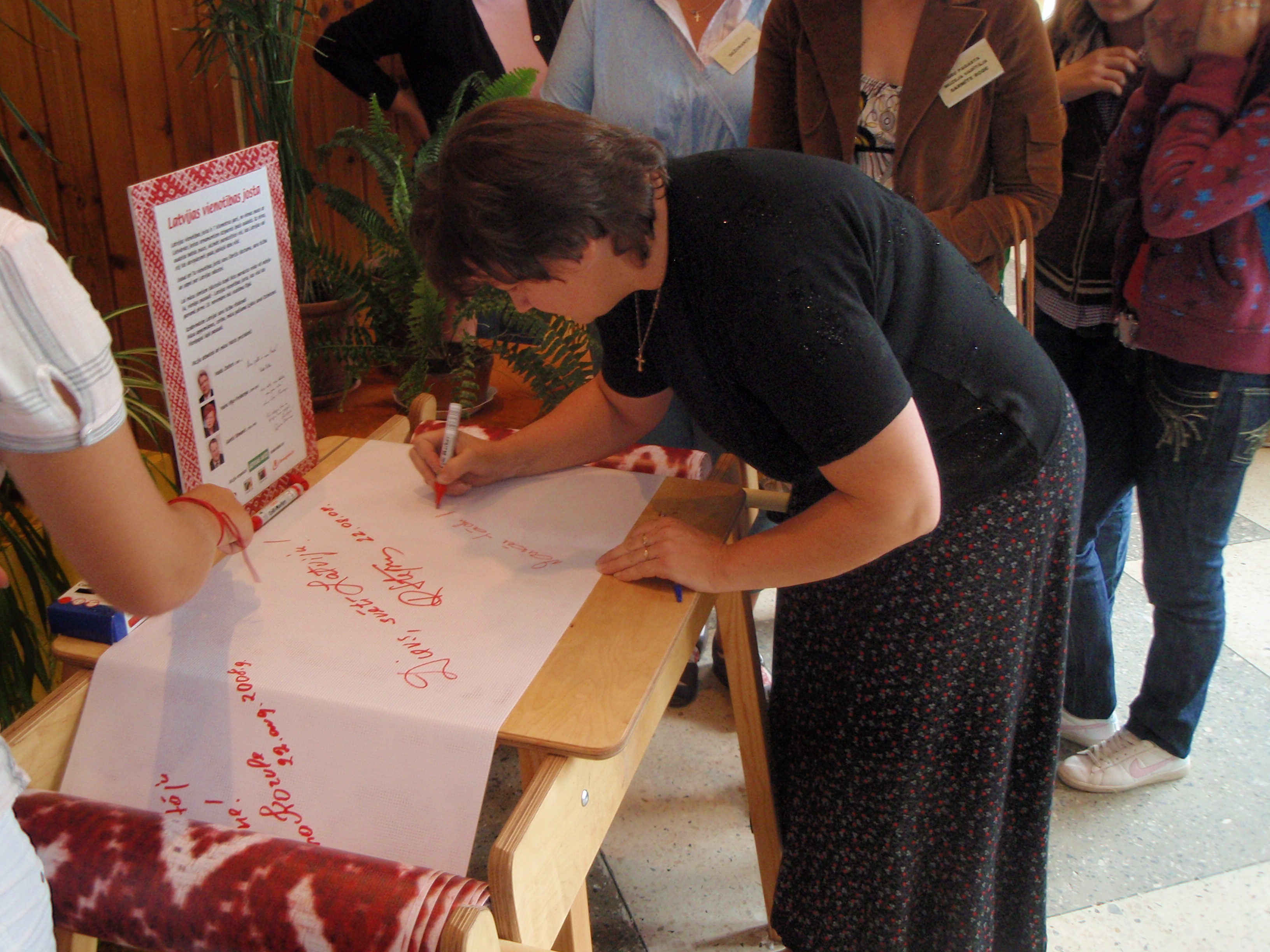 Bibliotēkas vadītāja Alita Kluša parakstās Vienotības jostā Aizkraukles rajona 7. Grāmatu svētku laikā